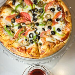 Shop1 Freshly baked pizza with olives, peppers, and cheese served with a glass of wine.